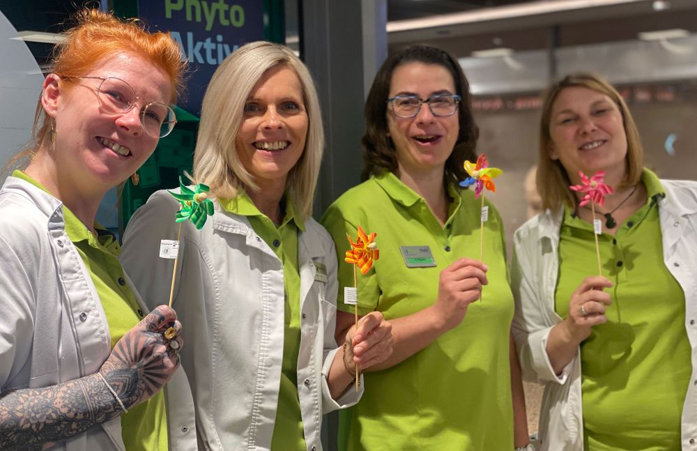 Apothekenteam in grünen Kitteln hält bunte Windräder