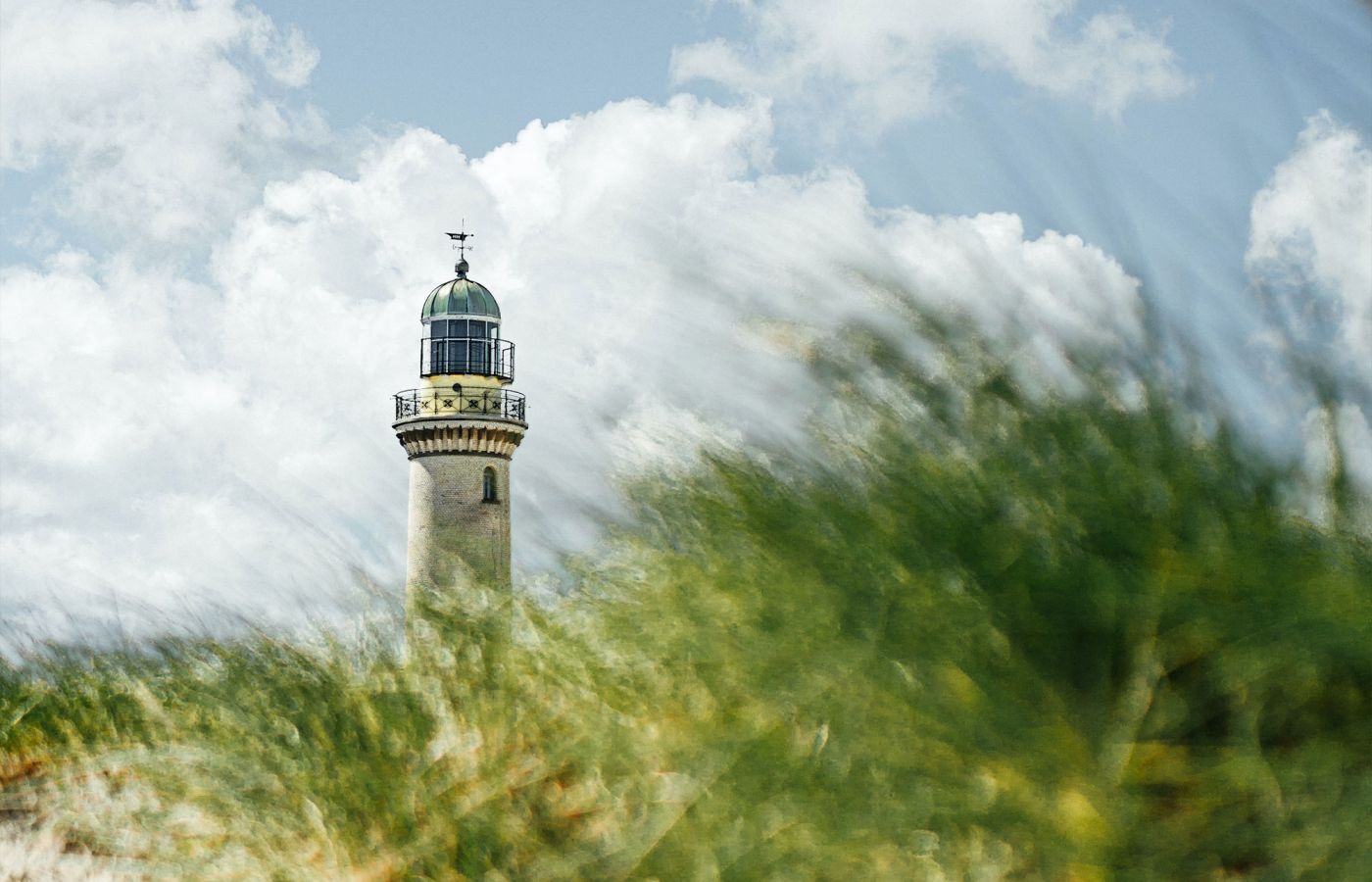 Leuchtturm ragt hinter unscharfen Gräsern vor bewölktem Himmel hervor